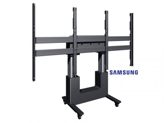 Mobile TV stand with wheels and sturdy black base, featuring vertical and horizontal mounting brackets for large flat-screen monitors; the word Samsung is partially visible behind the stand.
