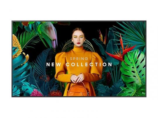 A woman in an orange dress holding a matching bag stands in front of colorful tropical leaves and flowers, with the text Spring New Collection shown on an 85-inch Samsung QB85C Smart Signage Display available for rent.