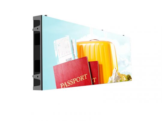 Rectangular digital display screen showing an image of travel essentials, including passports, boarding passes, and a yellow suitcase set against a blue sky background; the screen is angled to reveal its slim thickness.