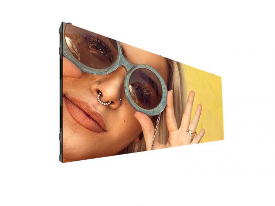 Close-up of a person wearing large round sunglasses and nose rings, holding up a peace sign against a bright yellow background, displayed on a digital screen.