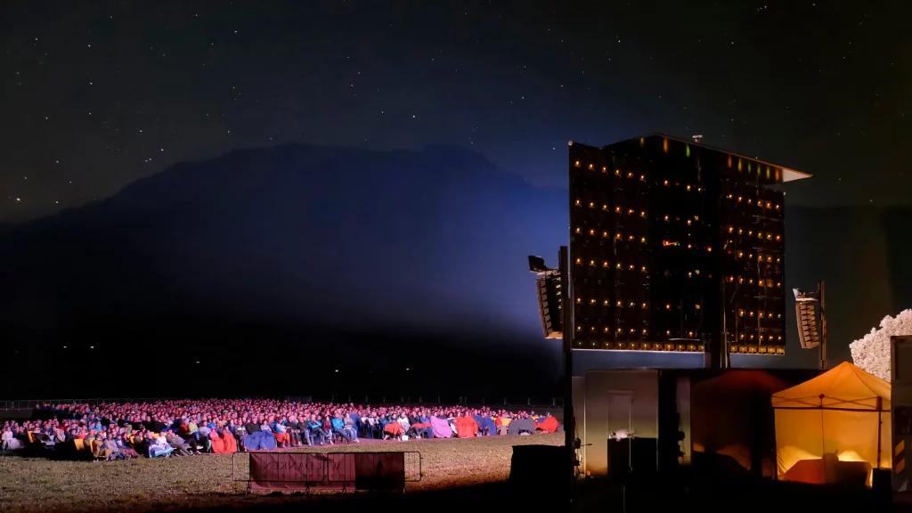 Große Menschenmenge sitzt nachts im Freien vor einer hell erleuchteten, hohen LED-Videowand zur Miete oder zum Kauf; im Hintergrund sind Berge und ein Sternenhimmel zu sehen.