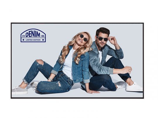 Ein Mann und eine Frau tragen lässige Denim-Mode - Jeansjacken, Jeanshosen und Sonnenbrillen - und sitzen nebeneinander auf dem Boden vor einem hellen Hintergrund. Im oberen linken Bildbereich ist das "Denim Limited Edition 1986"-Logo sichtbar.